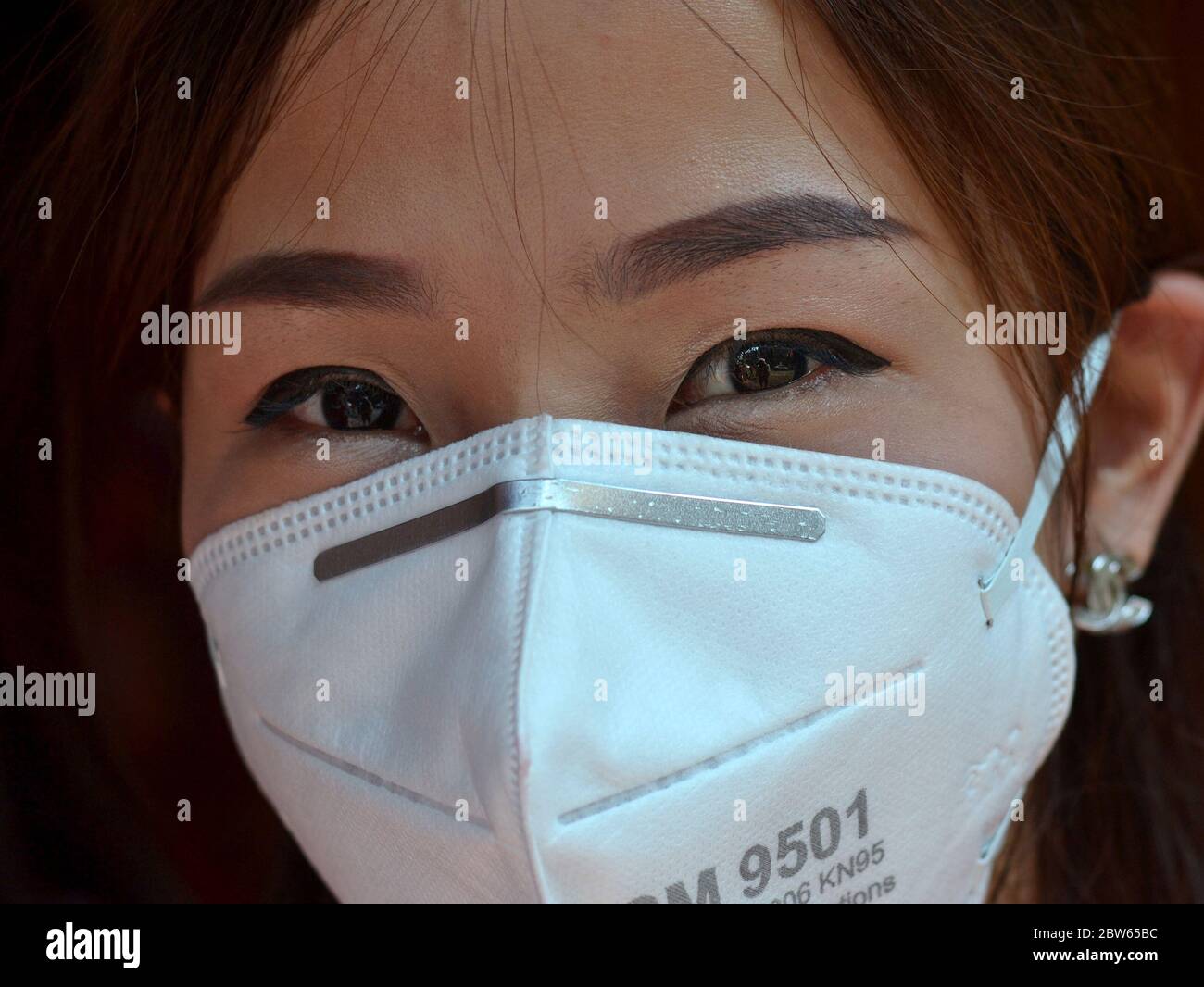 Thai girl with beautiful Asian eyes protects herself against air pollution with a white mouth mask. Stock Photo