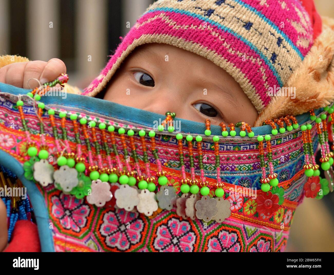 Cute Vietnamese Flower H’mong baby boy sits in an embroidered, traditional baby sling and looks at the camera. Stock Photo