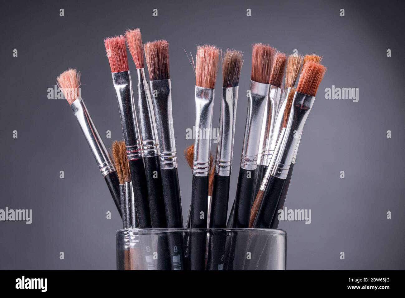 Black brushes inside a glass container against a grey background Stock Photo