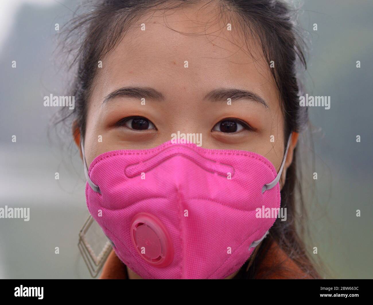 Young Vietnamese woman wears a pink protective face mask with breathing valve during the 2019/20 corona-virus pandemic. Stock Photo
