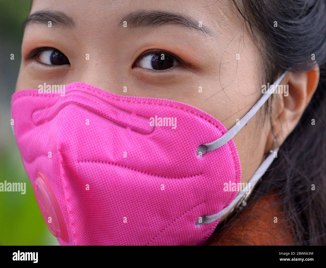 Young Vietnamese woman wears a pink ear loop face mask with breathing valve during the 2019/20 corona virus pandemic. Stock Photo
