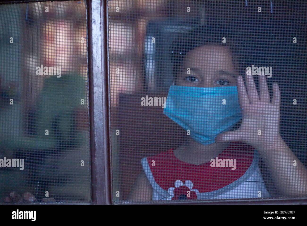 Little child looking outside from the door of home with mask on face with a hope of ending Pandemic Corona virus Stock Photo