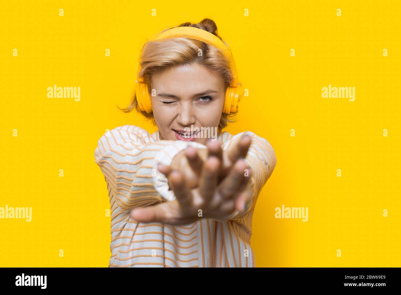 Caucasian woman with blonde hair listening to music on a yellow wall ...