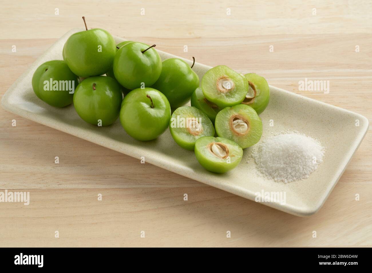 Dish with fresh green whole and half Can Erik plums and a bowl with salt Stock Photo
