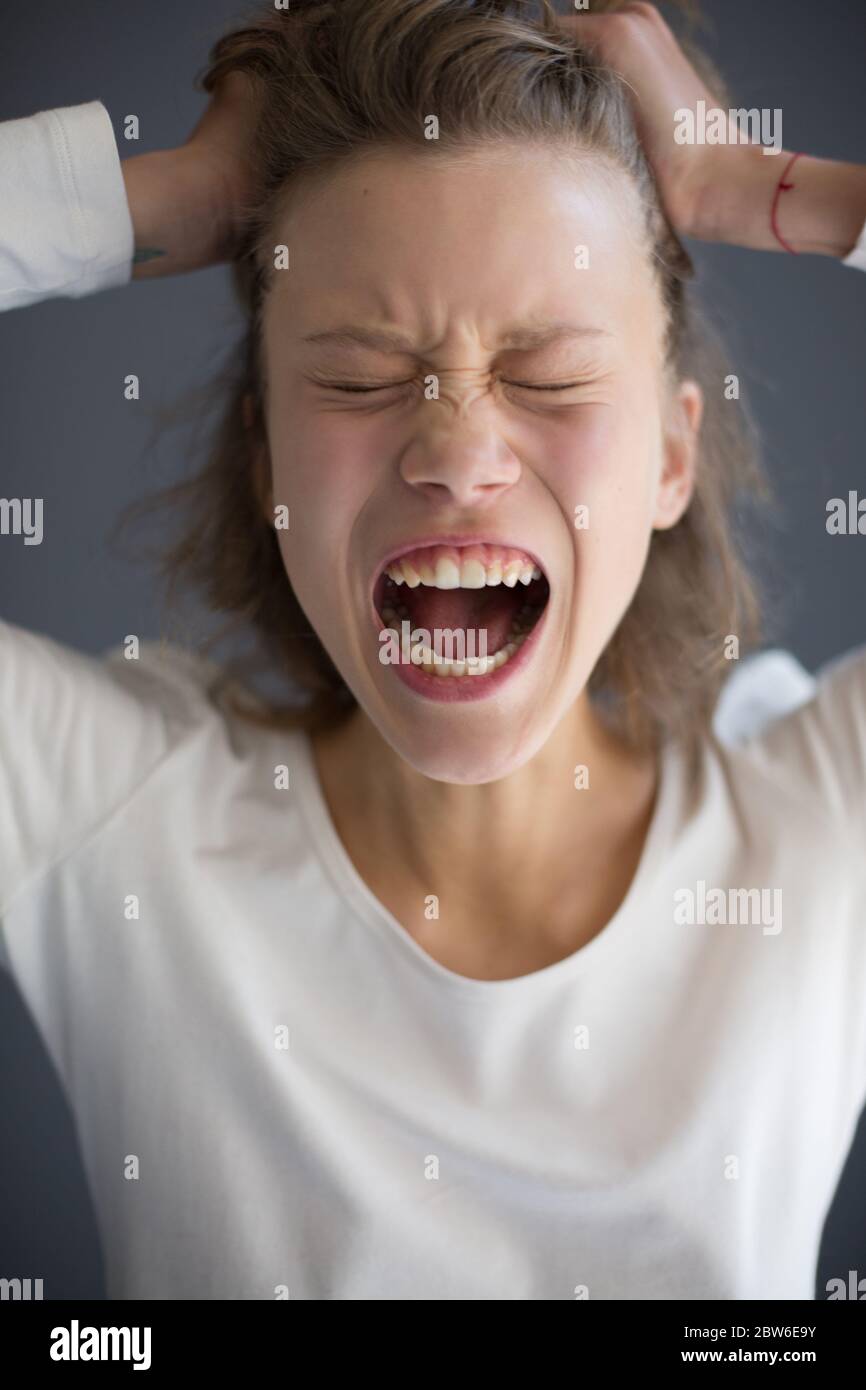 Portrait of young screaming lady holding hands on her head and closing