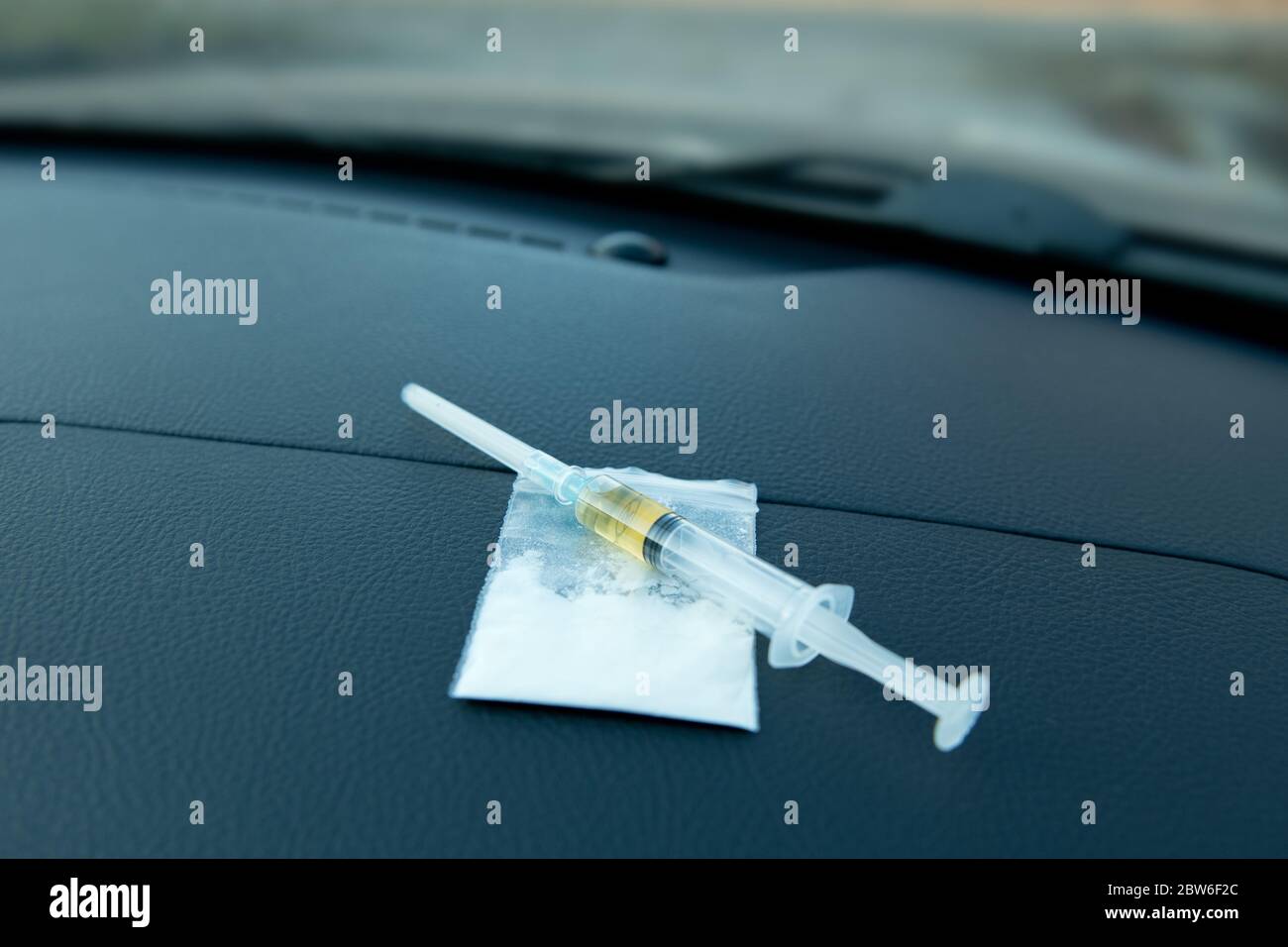 a syringe and a bag with a dose of the drug lie on the dashboard of the car Stock Photo