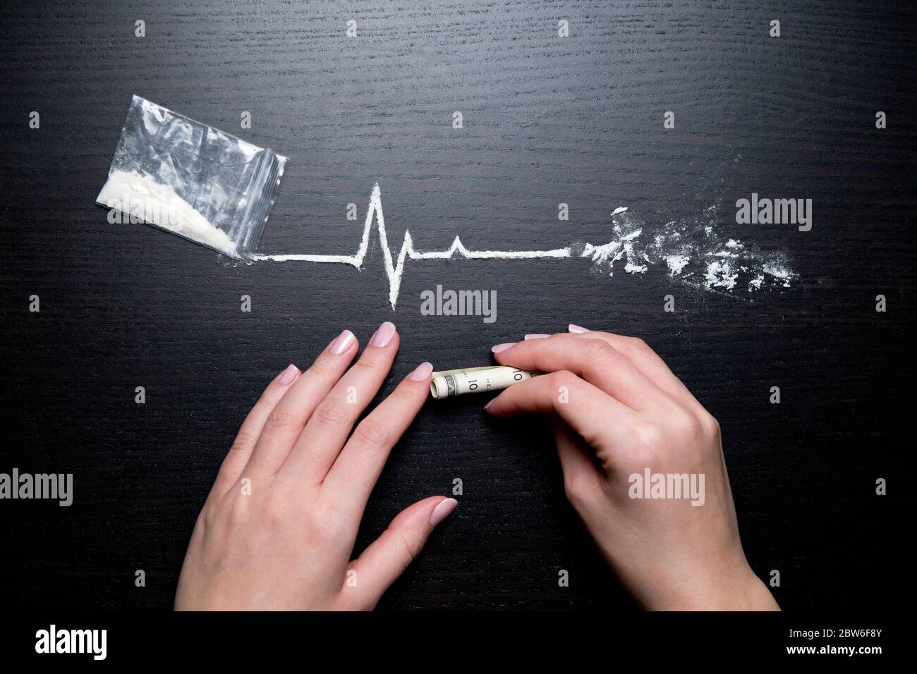 female hands, dollar and cocaine in the form of a heartbeat line on a black table Stock Photo