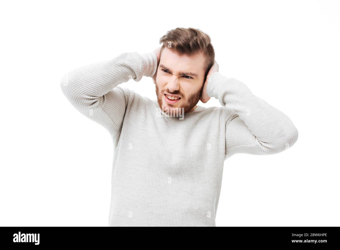 Handsome man covering ears because of loud noise over white background. Guy can't stand the sound isolated Stock Photo