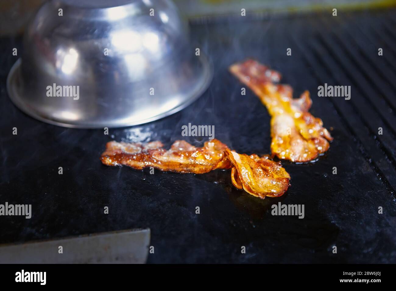 Bacon strips frying on pan in restaurant for dinner.Unhealthy fat pork