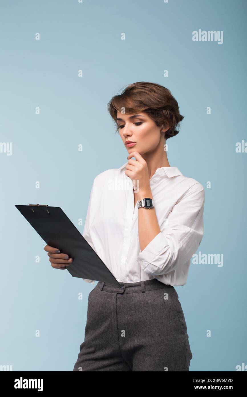 Young beautiful business woman with dark short hair in white shirt  thoughtfully looking on folder with documents over blue background isolated  Stock Photo - Alamy