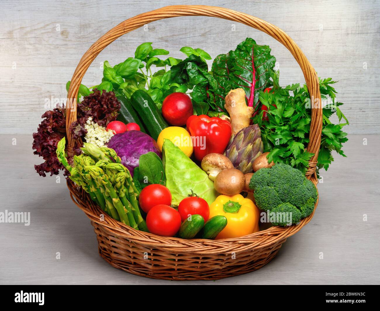 Vintage basket filled with an arrangement of mixed colorful vegetables on light background, looking fresh, healthy and appetizing, a whole food nutrit Stock Photo