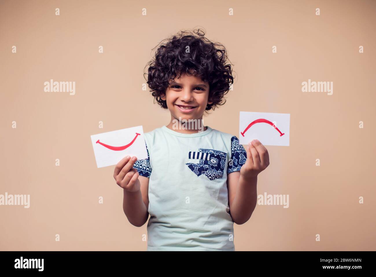 A portrait of kid boy holding cards with positive and negative symbol ...