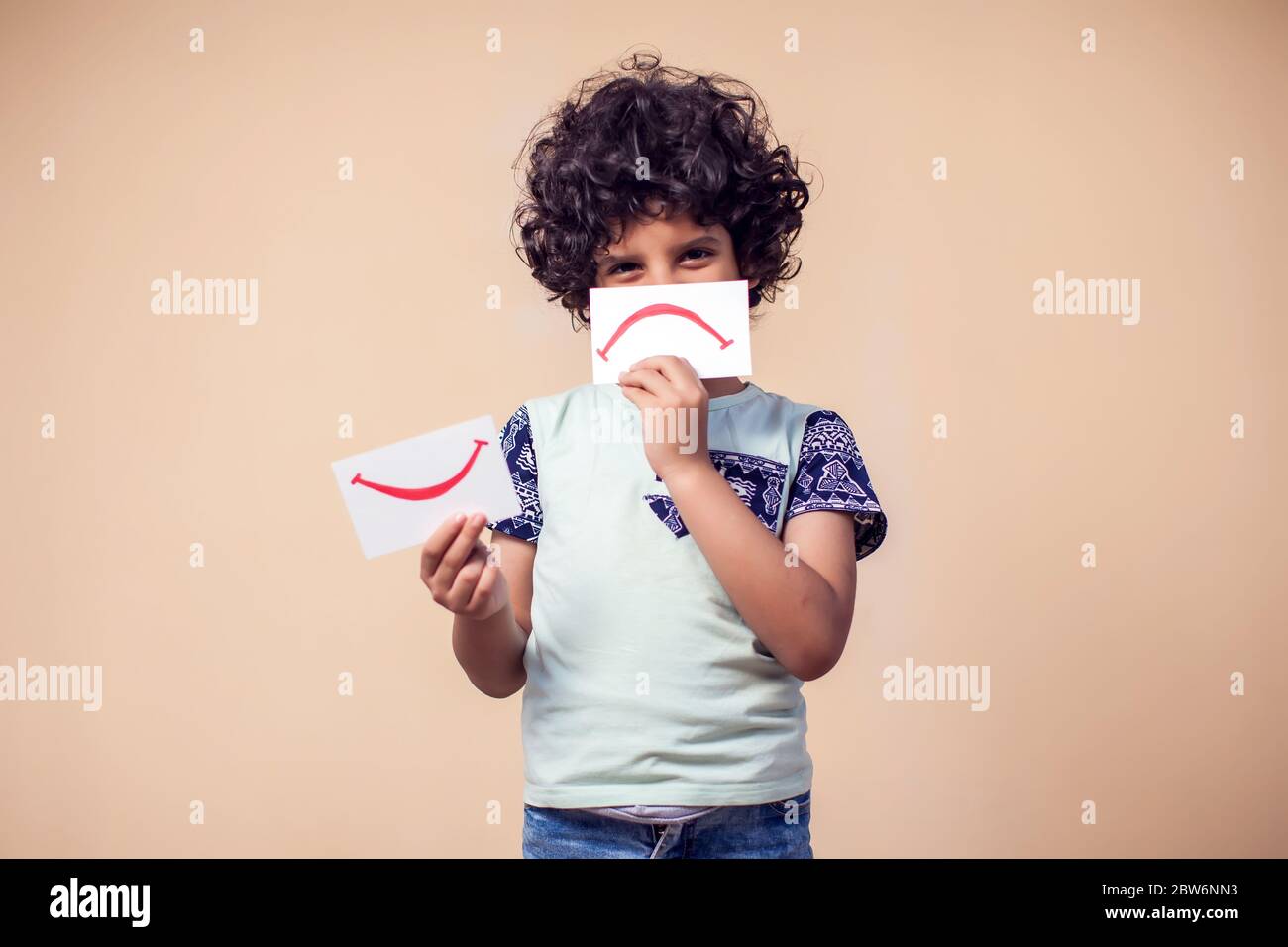 A portrait of kid boy holding cards with positive and negative symbol. Children and emotions concept Stock Photo