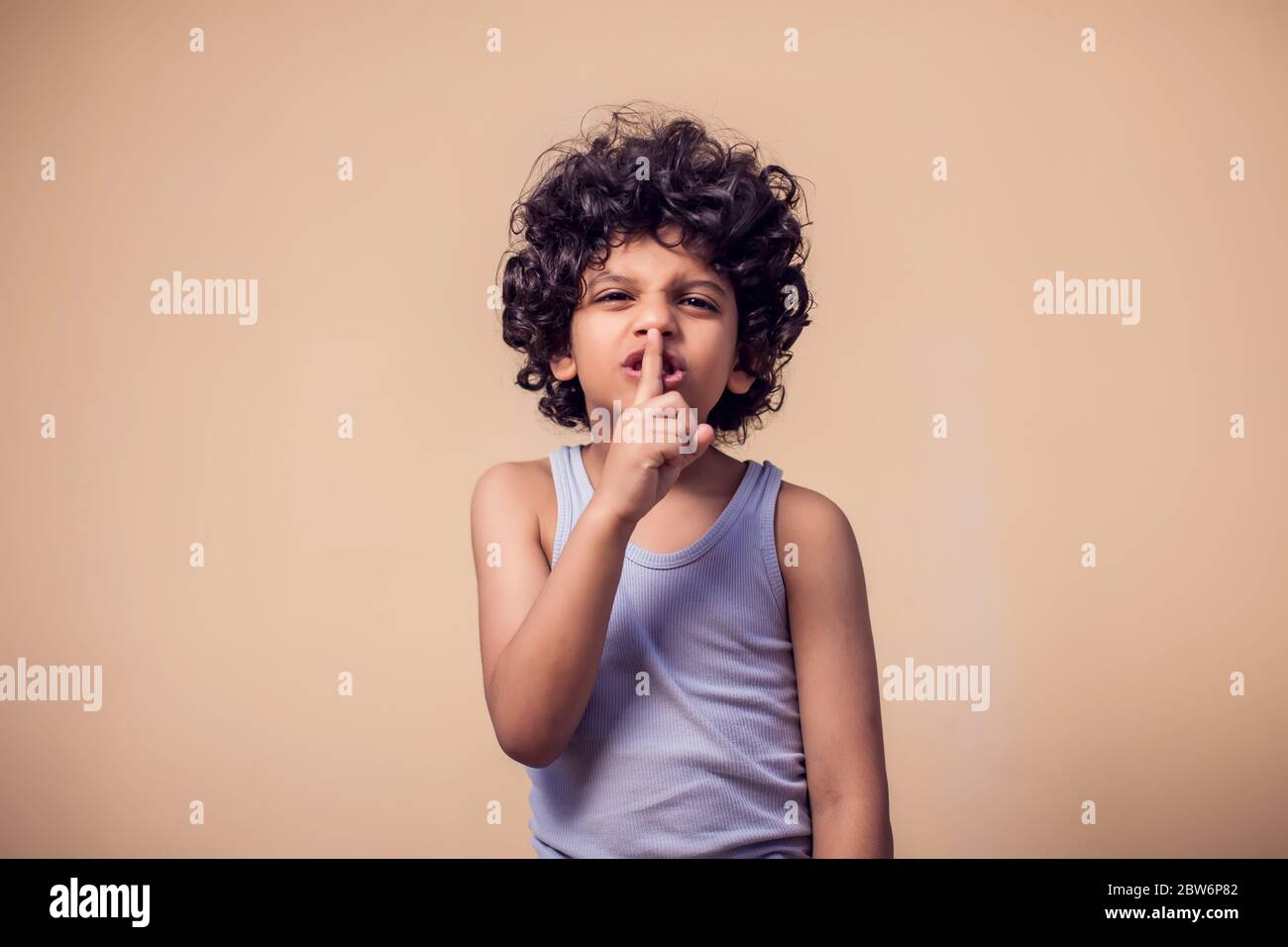 A portrait of kid boy with curly hair showing secret gesture. Children and emotions concept Stock Photo