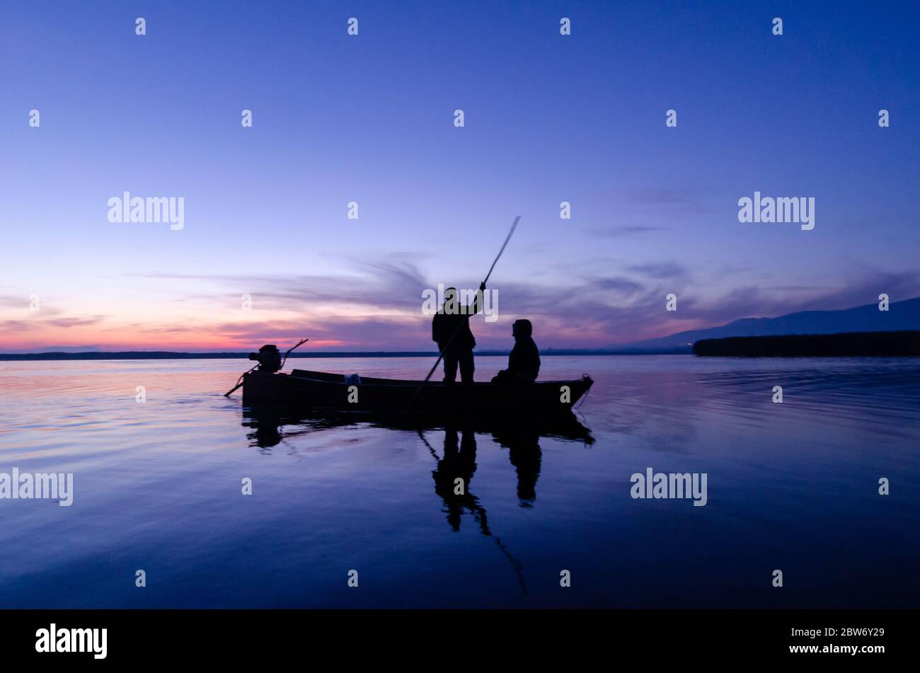 Silhouette of fishing boat and fisherman in the sunrise on the lake in ...