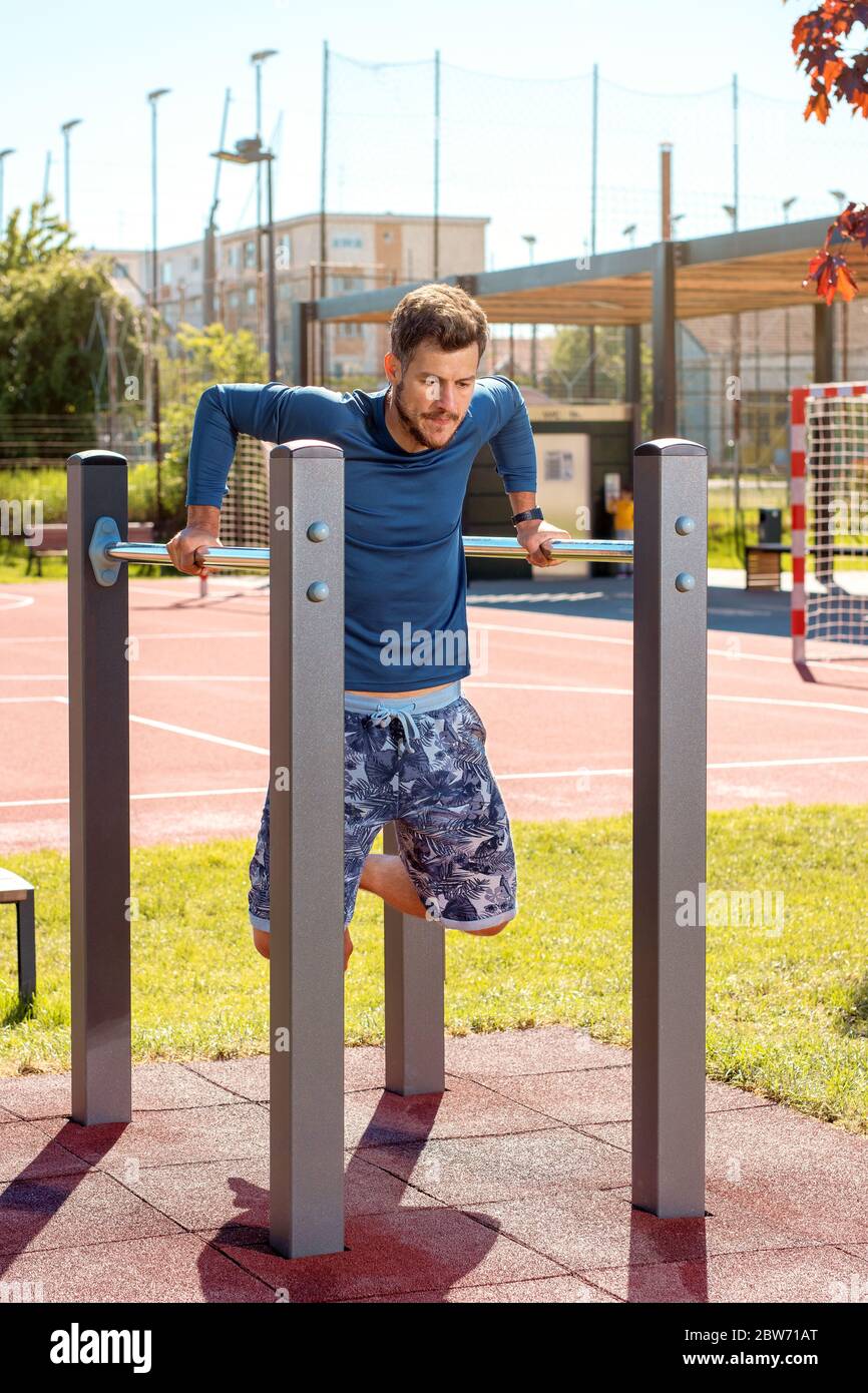 Young handsome man training at parallel bars in the playground on a sunny day Stock Photo