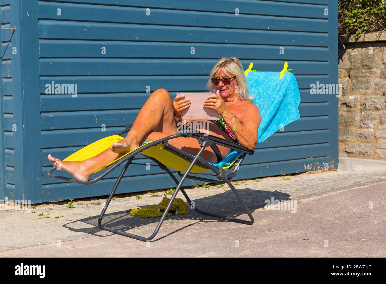 Bournemouth, Dorset UK. 30th May 2020. UK weather: hot sunny day at Bournemouth beaches as the glorious weather continues and temperatures rise with clear blue skies and unbroken sunshine. Sunseekers head to the seaside early to get a good spot and enjoy the sunshine, as the beaches are expected to get packed later. Joan soaks up the sun rays at her beach hut. Credit: Carolyn Jenkins/Alamy Live News Stock Photo