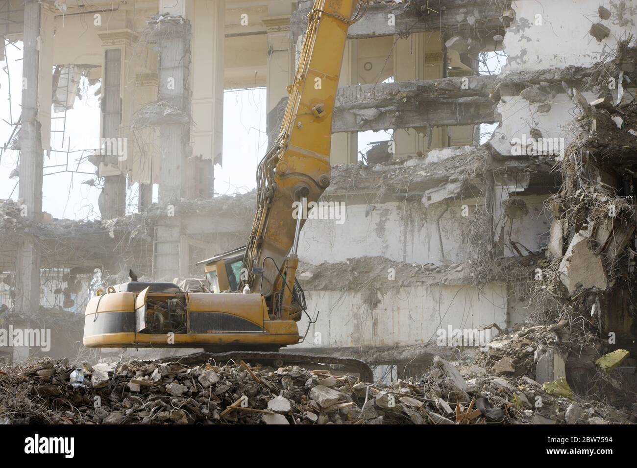 Closeup of special hydraulic excavator-destroyer during operation, concrete dust in the air, ruins of a building on background. Ultra high demolition Stock Photo