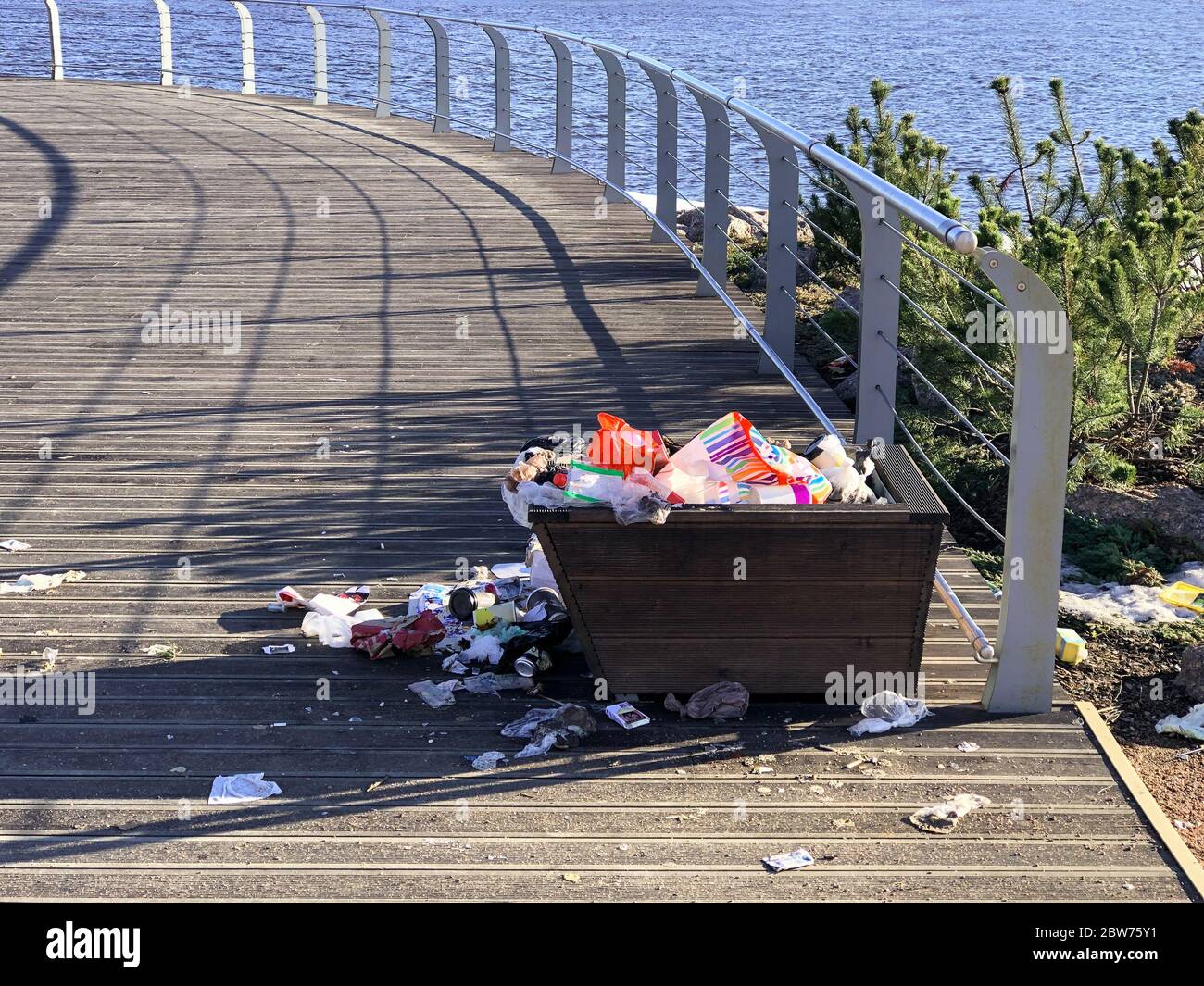 Overflowing trash can on the waterfront in the recreation area. Garbage bin. Pile of plastic garbage waste on the floor. Stock Photo