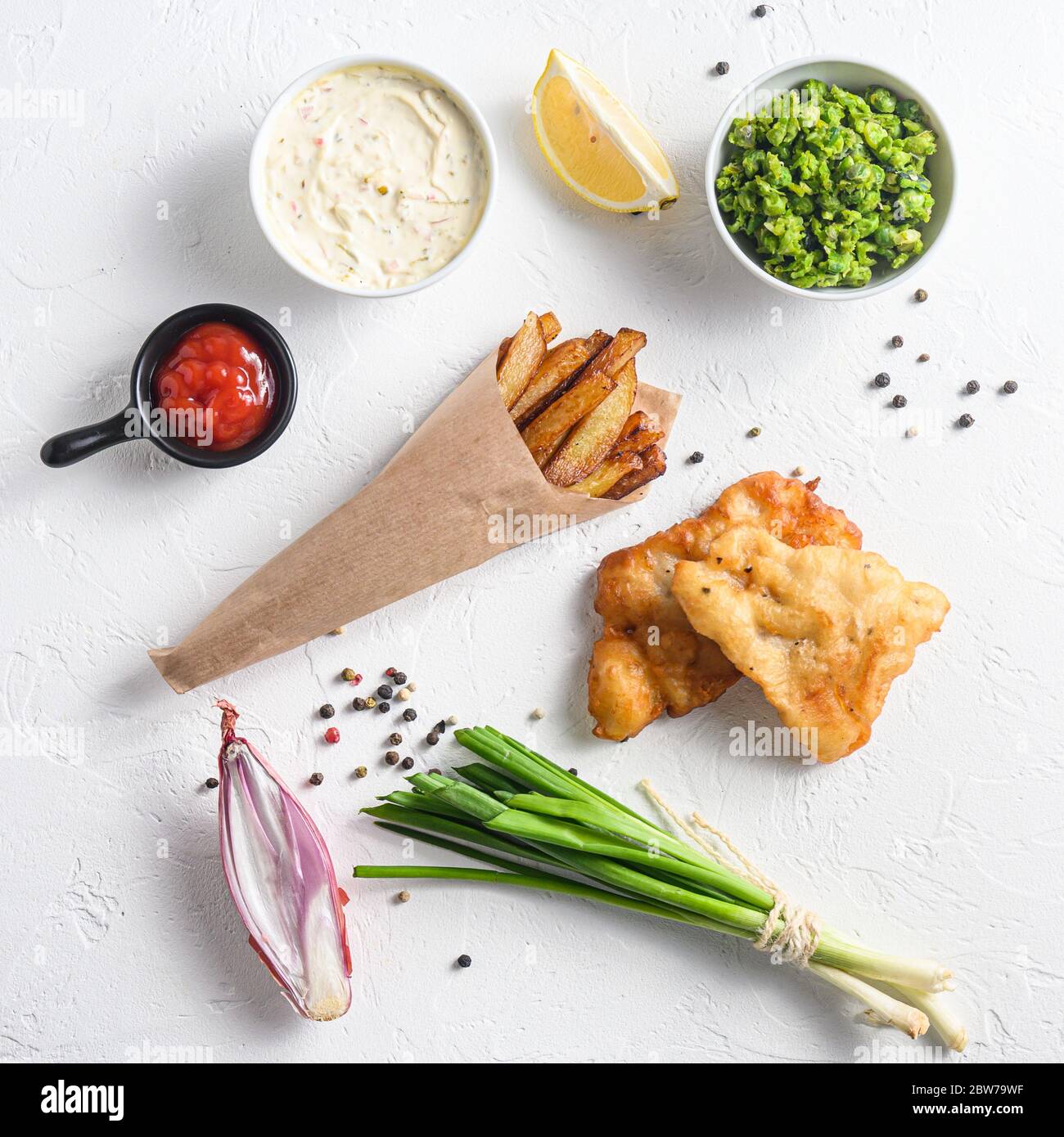 Fried fish and chips in a paper cone on white background with all