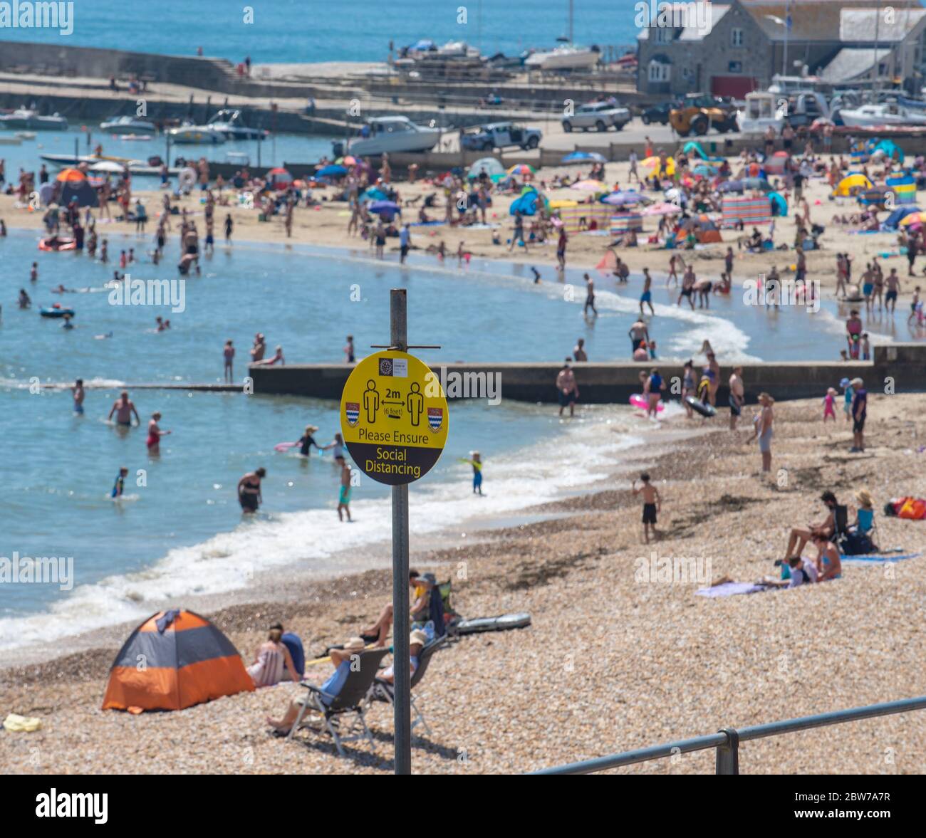 Lyme Regis, Dorset, UK. 30th May 2020. UK Weather. Social distancing reminder signs at Lyme Regis where beachgoers and families packed the beach this afternoon to bask in the hot afternoon sunshine on the hottest day of the year. Credit: Celia McMahon/Alamy Live News. Stock Photo