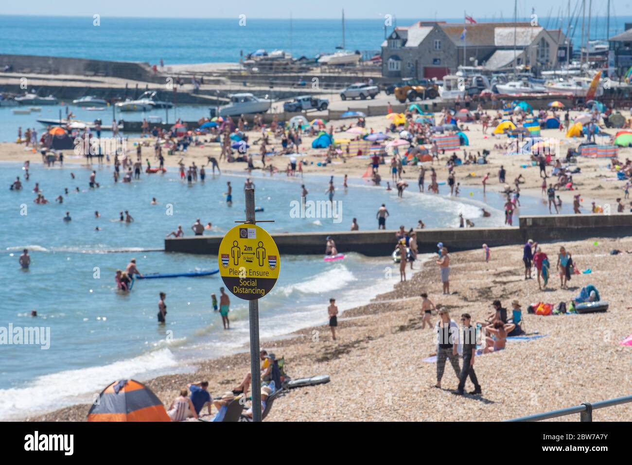 Lyme Regis, Dorset, UK. 30th May 2020. UK Weather. Social distancing reminder signs at Lyme Regis where beachgoers and families packed the beach this afternoon to bask in the hot afternoon sunshine on the hottest day of the year. Credit: Celia McMahon/Alamy Live News. Stock Photo