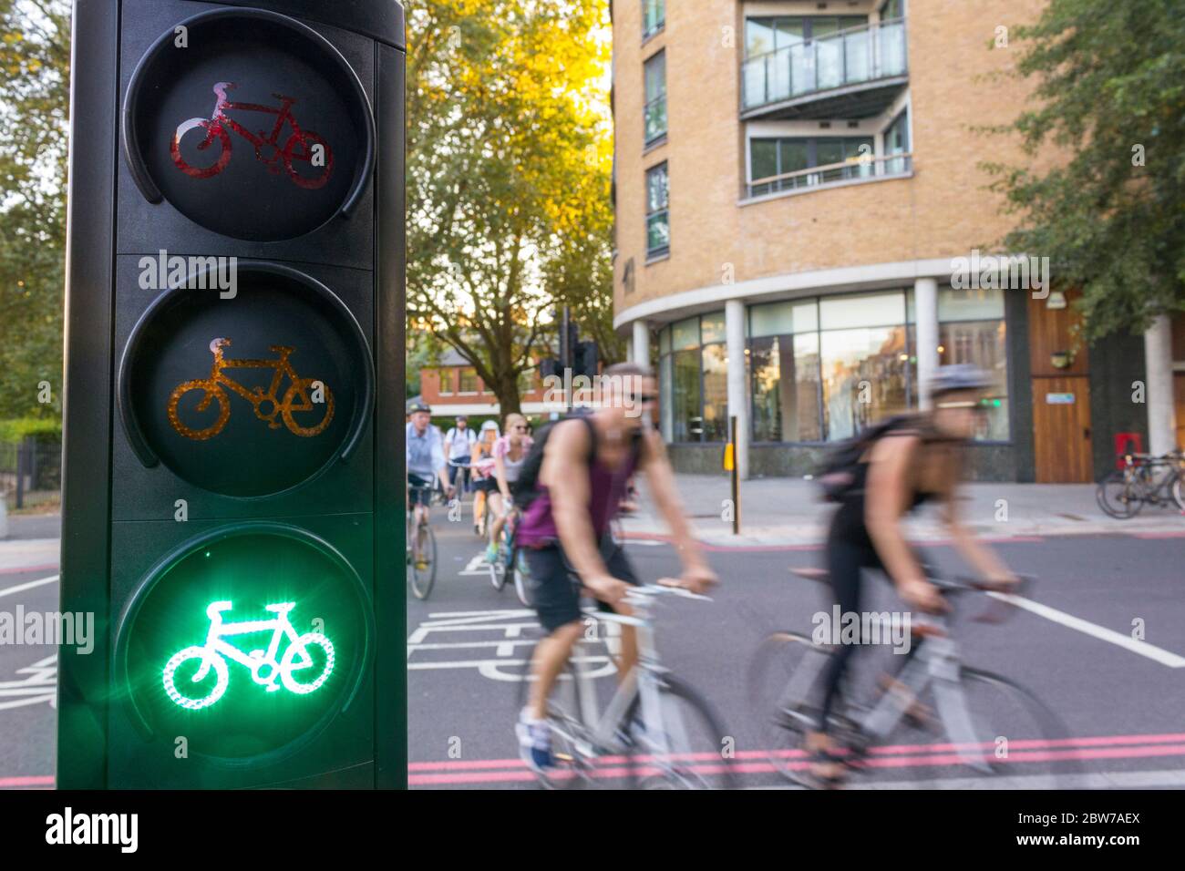 A number of cycle commuters cross a road on a dedicated cycle crossing in London, with a green cycle light in the foreground. Stock Photo