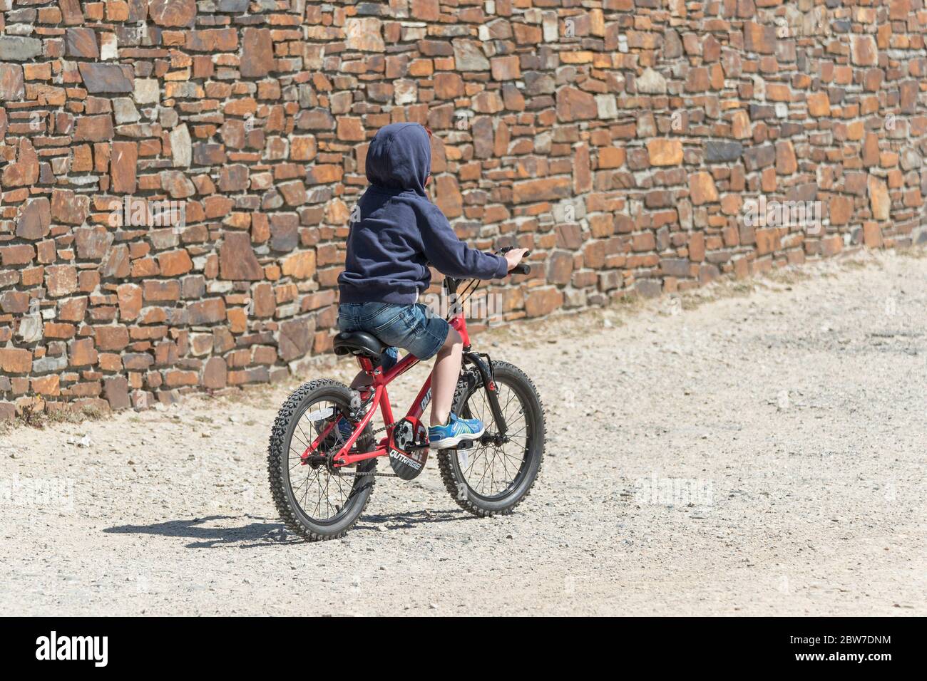 A young boy wearing a hoodie riding his bicycle. Stock Photo