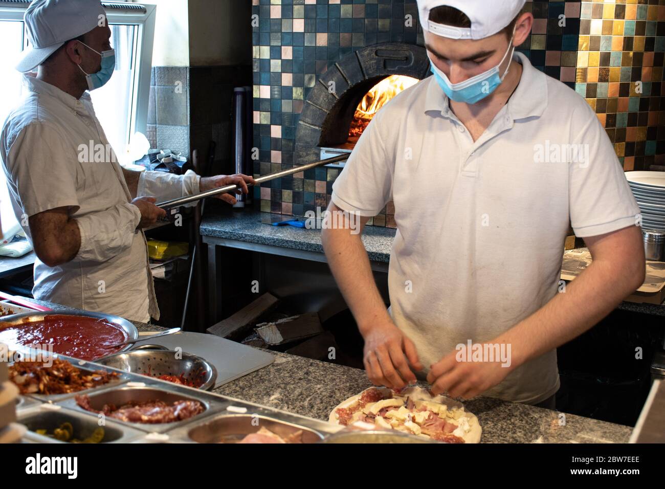 Chefs preparing pizza in a pizzeria wearing masks and protections during covid or coronavirus emergency, reopening pizzerias and restaurants Stock Photo
