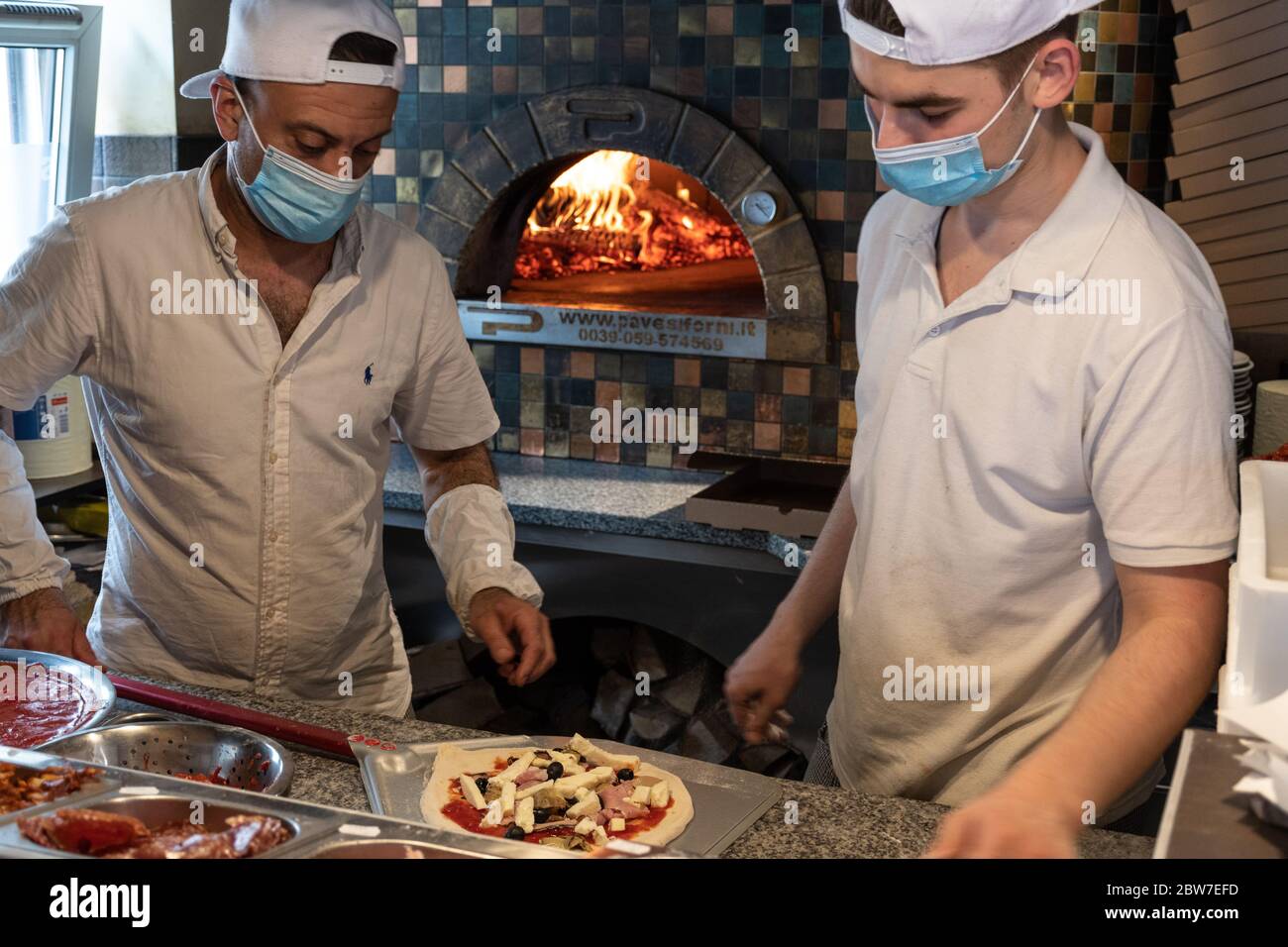 Chefs preparing pizza in a pizzeria wearing masks and protections during covid or coronavirus emergency, reopening pizzerias and restaurants Stock Photo