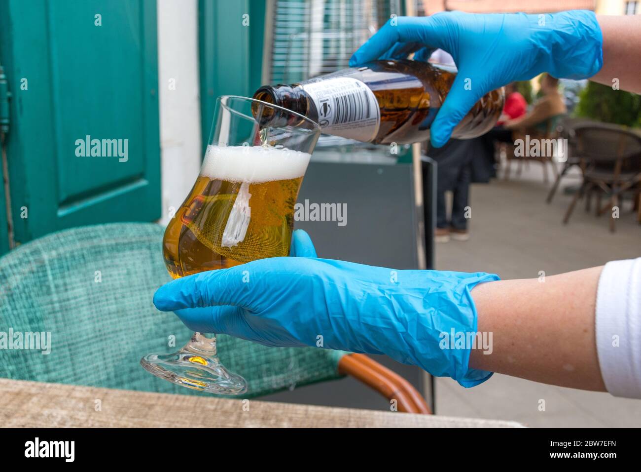 Hands of waiter or waitress dressing plastic gloves serving beer to the client at the table of an outdoor bar, cafe or restaurant, reopening Stock Photo