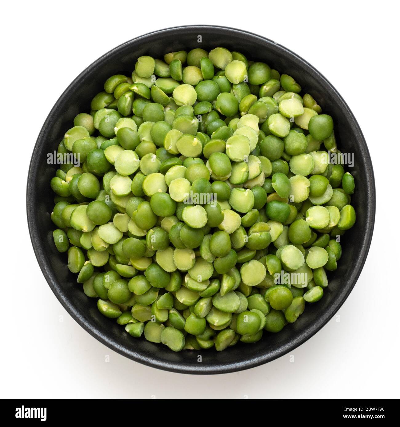 Dried green split peas in a black ceramic bowl isolated on white.Top
