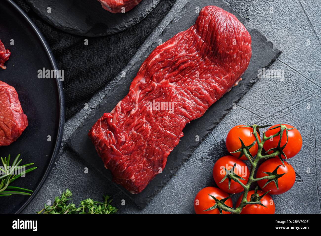 Raw tri tip cut black angus organic steak on a black plate and stone