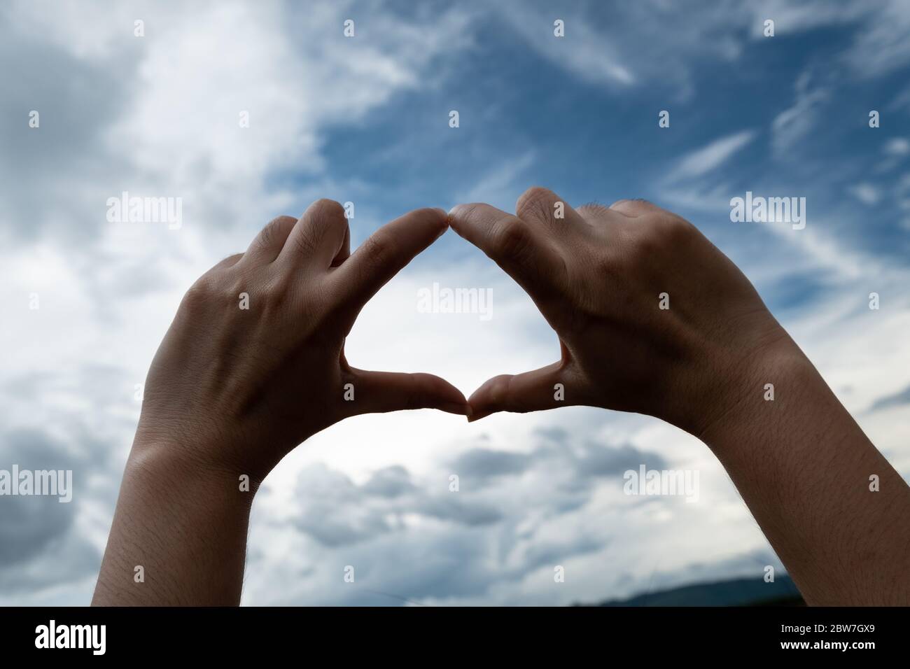 Woman making a heart shaped with her hands on blue sky and cloud ...