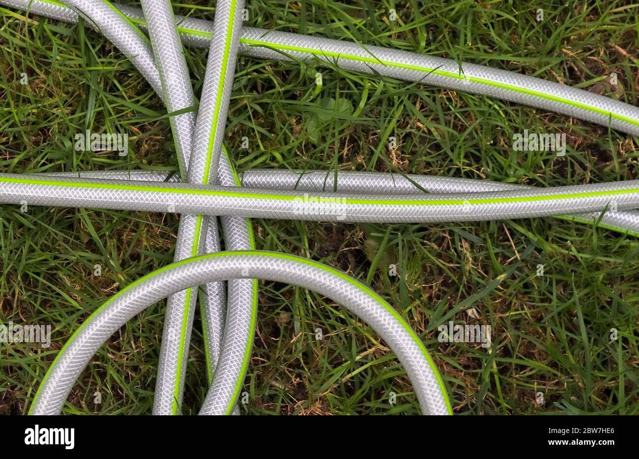 Top view of hosepipe on grass and cobblestone surfaces. Minimalistic conception. Stock Photo