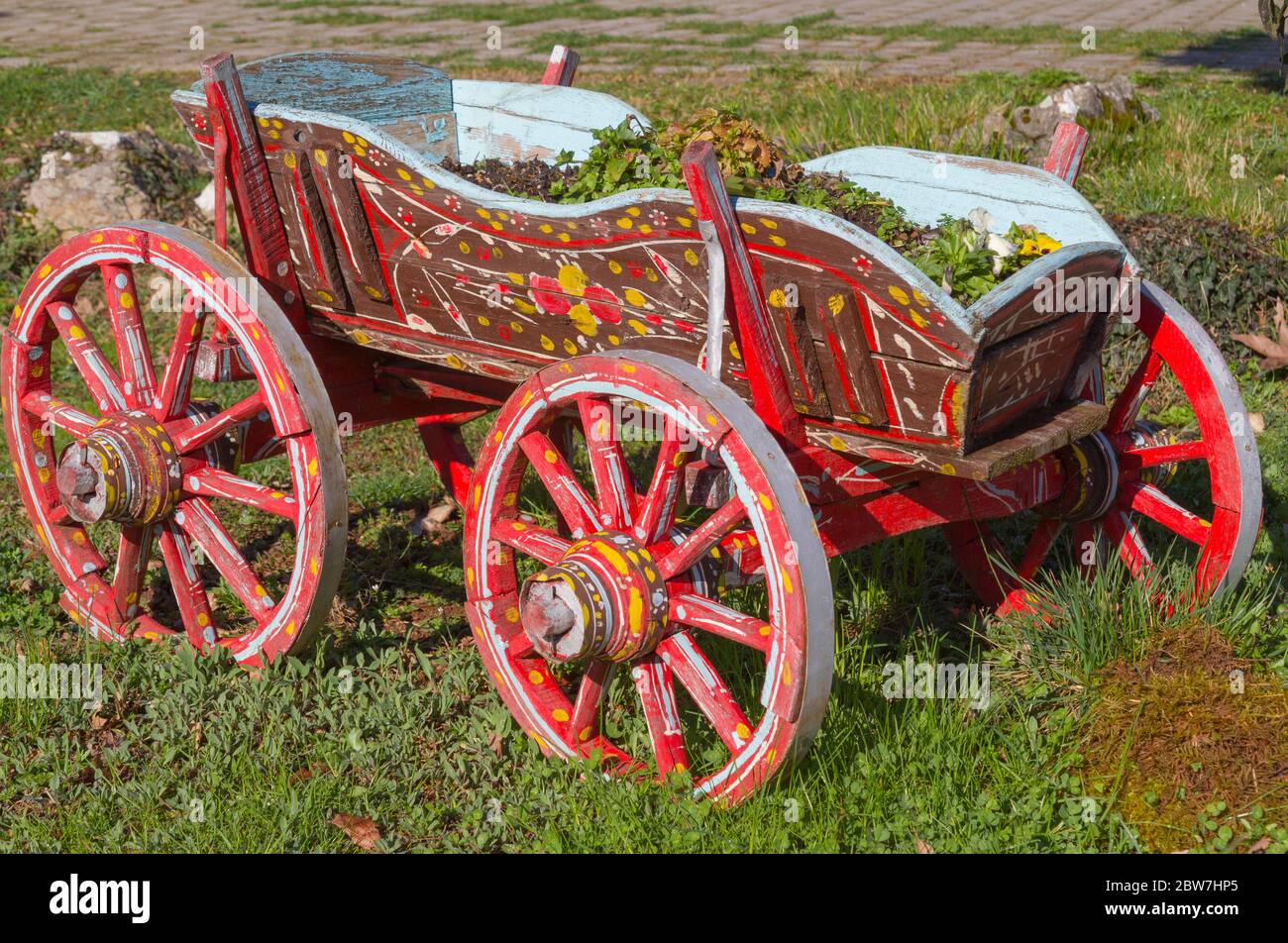 Karpenissi, Greece. A colorful old cart on the grass. Painted with brown, red, yellow, green, light blue colors. It contains soil and leaves. Stock Photo