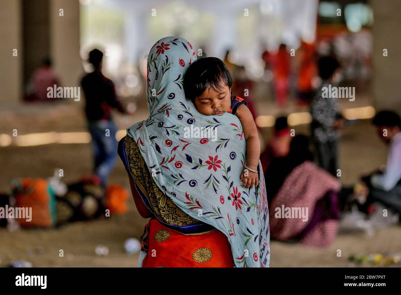 A woman and her tired daughter seen under a flyover waiting for transportation. Due to massive job losses after the lockdown put in place to contain the coronavirus pandemic, most migrant workers with their families are returning to their villages. Stock Photo