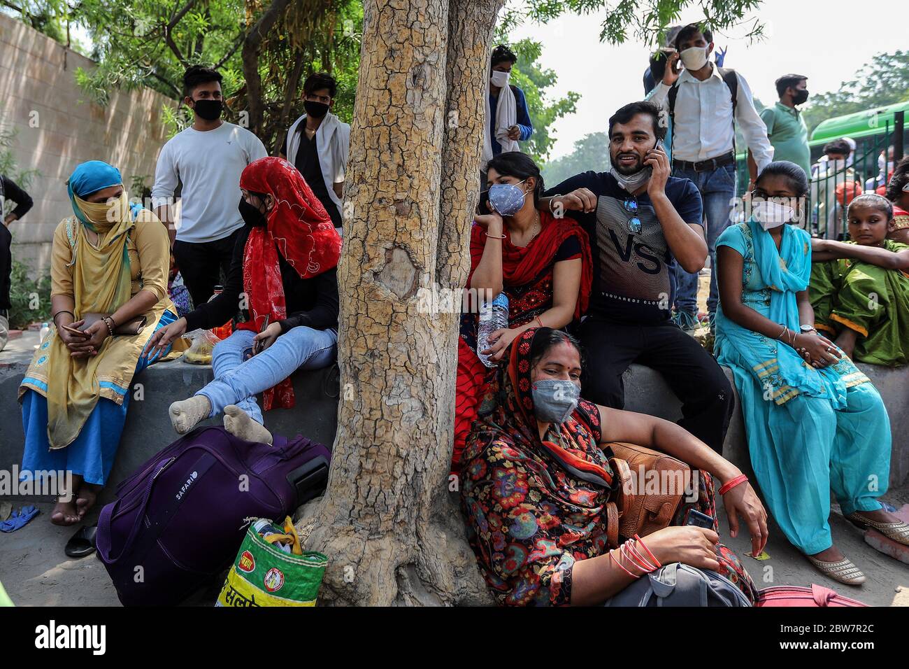 Migrants wait outside a government school to get screened before boarding buses for the Anand Vihar Railway Station. Due to massive job losses after the lockdown put in place to contain the coronavirus pandemic, most migrant workers with their families are returning to their villages. Stock Photo