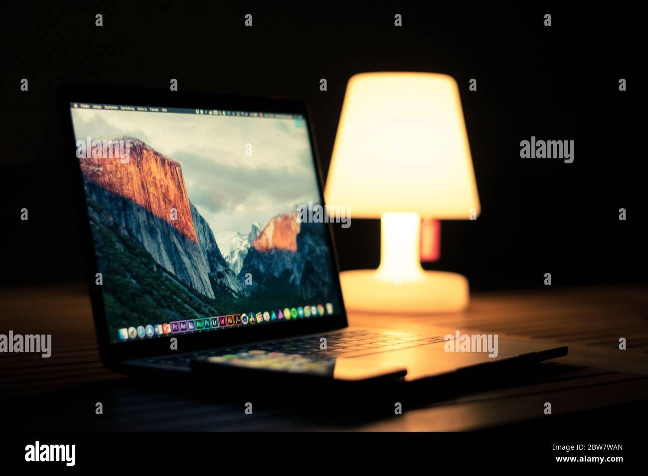 iPhone  auf einem aufgeklappten MacBook Pro in der Dämmerung mit Lampe im Hintergrund Stock Photo
