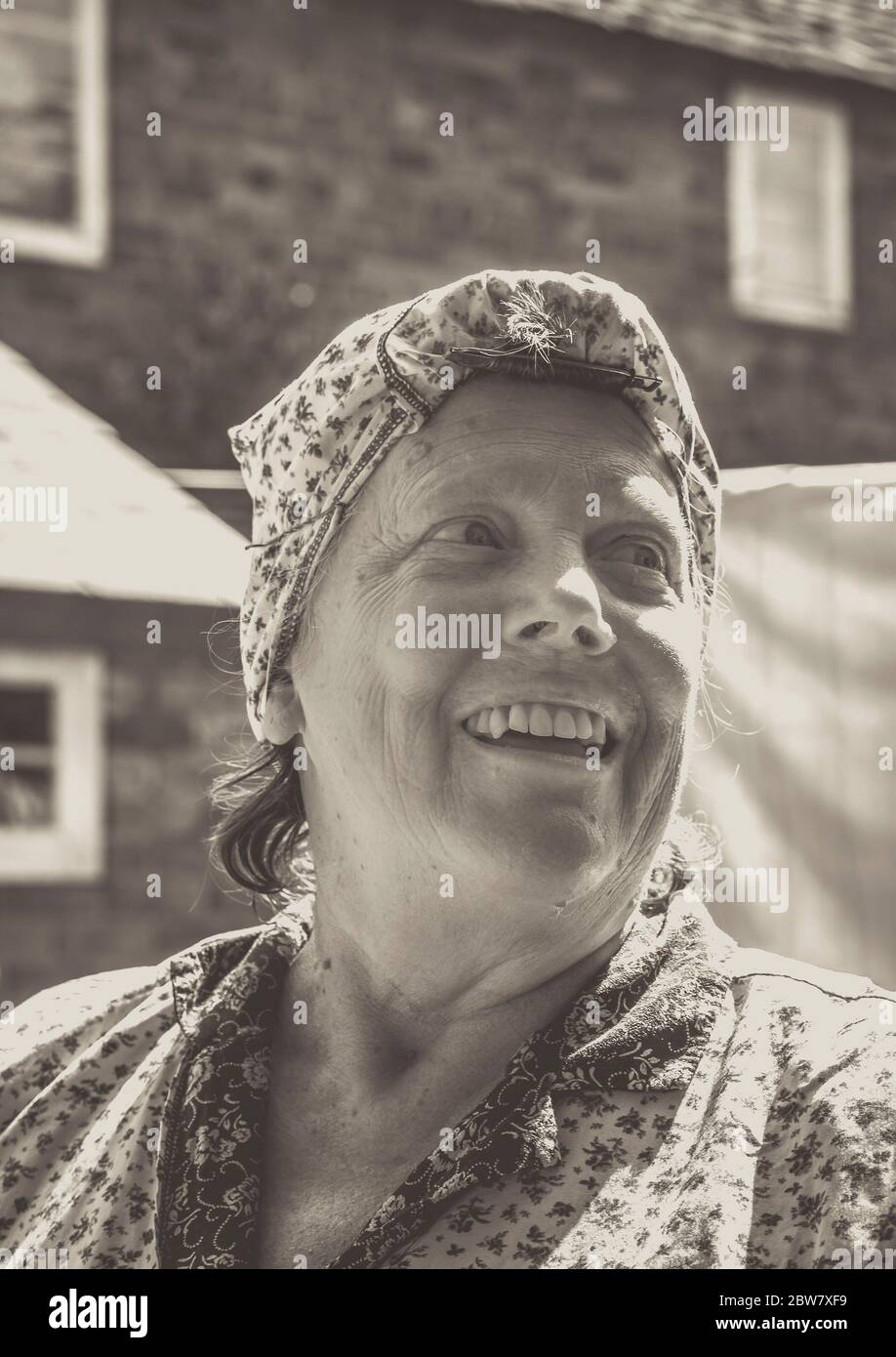 Monochrome close up of smiling 1940s woman, vintage housewife, isolated outdoors in overalls doing laundry housework in sunshine, 1940s WWII event, UK. Stock Photo