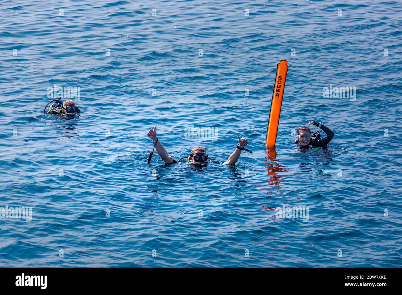 Scuba divers makes the ok sign in tropical sea. Scuba sign, surface marker buoy. Surface of the blue ocean, team of divers on surface of the sea Stock Photo