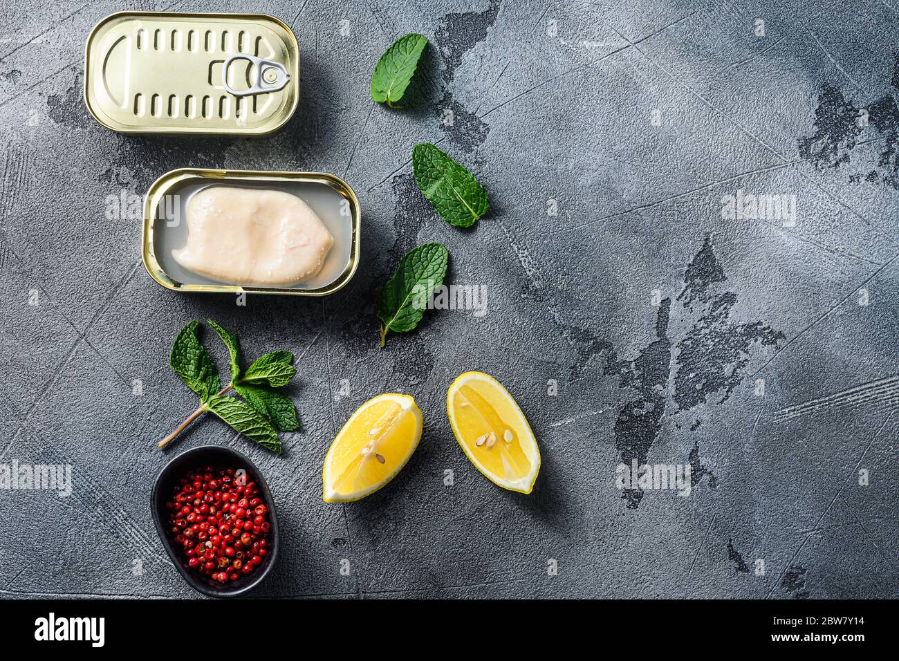 canned squid, set of opened cans closed conserve with fresh leaves and lemon with rose pepper over grey background top view spacr for text. Stock Photo