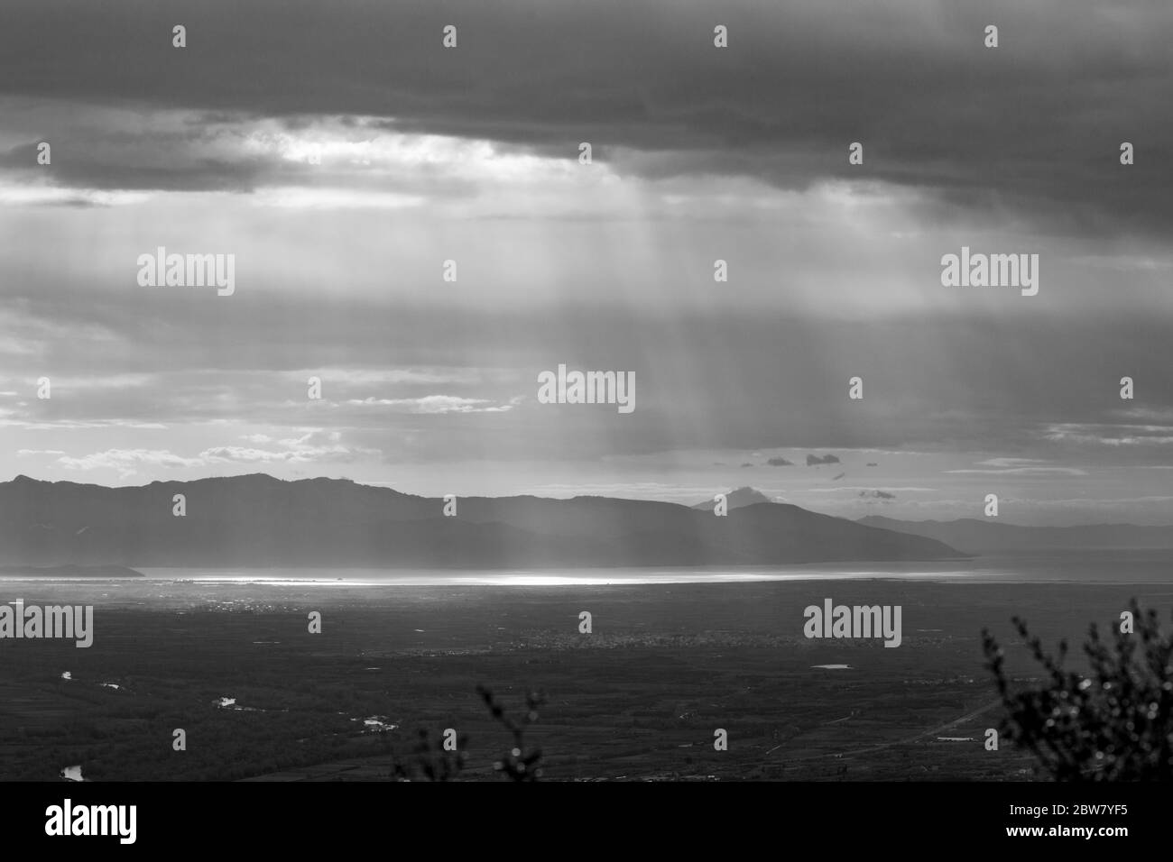 Sun rays make their way through heavy clouds over the sea in Northern Greece. High angle view from the mountains at the Greek region of Xanthi. Black and white travel photo Stock Photo