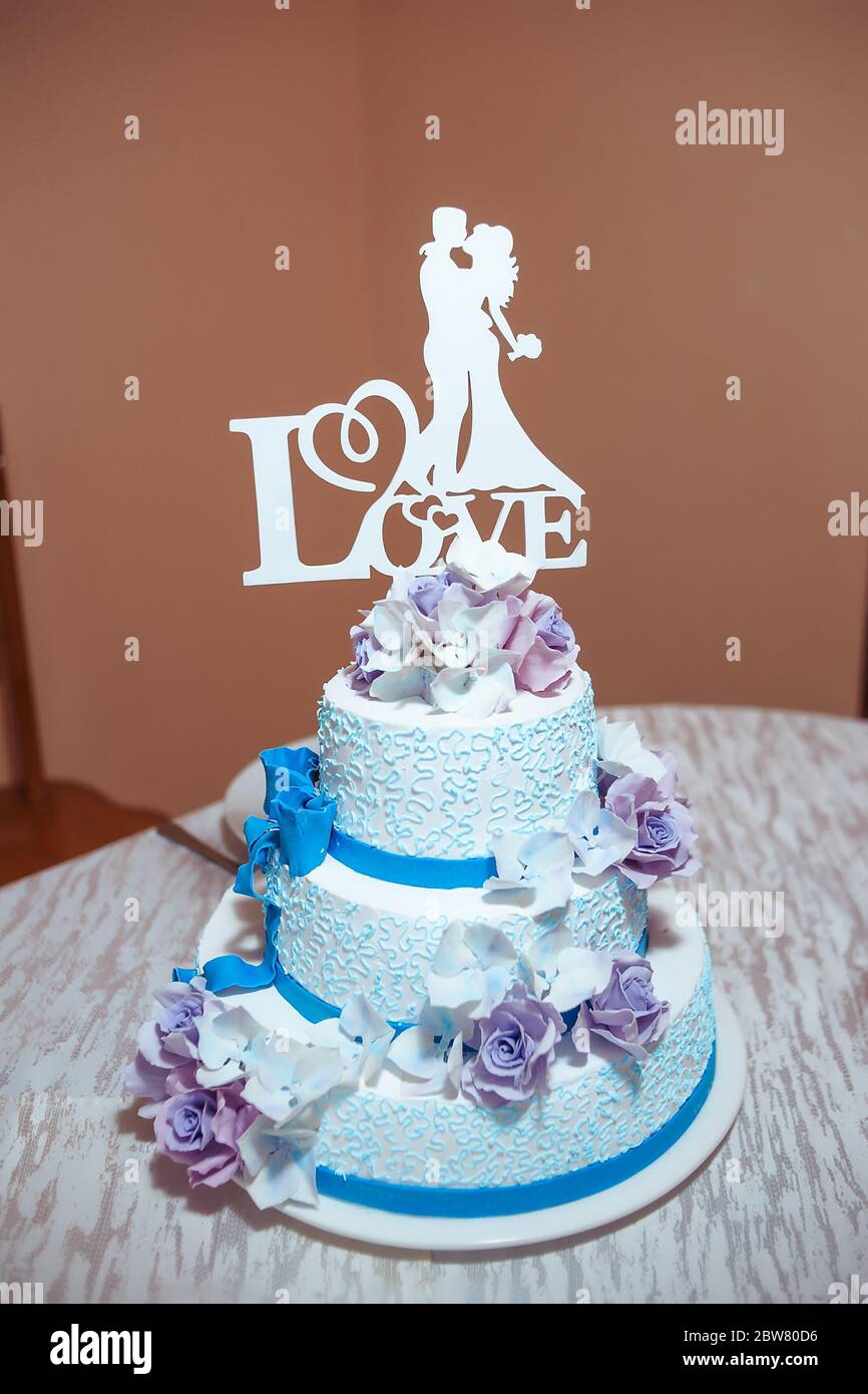 A beautiful blue wedding cake decorated with creamy white and purple flowers with the silhouette of a bride and groom. I love you inscription. Stock Photo