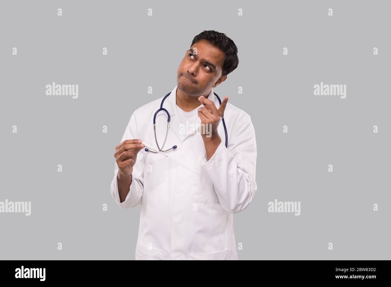 Doctor Watching Thermometer Thinking Isolated. Indian Man Doctor Analysing with Thermometer in Hands. Healthy Life, Doctor, Virus Concept Stock Photo