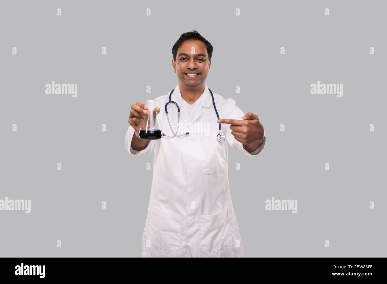 Male Doctor Pointing at Flask with Colorfull Liquid Isolated. Science, Medical, Virus Concept. Indian Man Doctor Smilling. Stock Photo