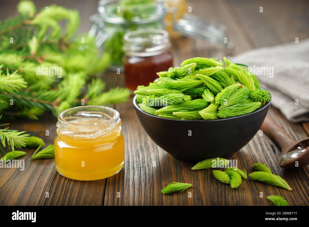 Jar of honey or syrup, spruce tips in a black bowl, twigs of fir tree on wooden table. Stock Photo
