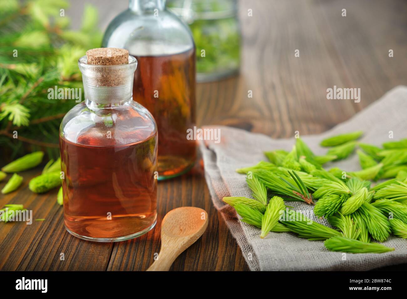 Bottles of potion, syrup or honey from fir buds and needles, twigs of fir tree on wooden table. Stock Photo