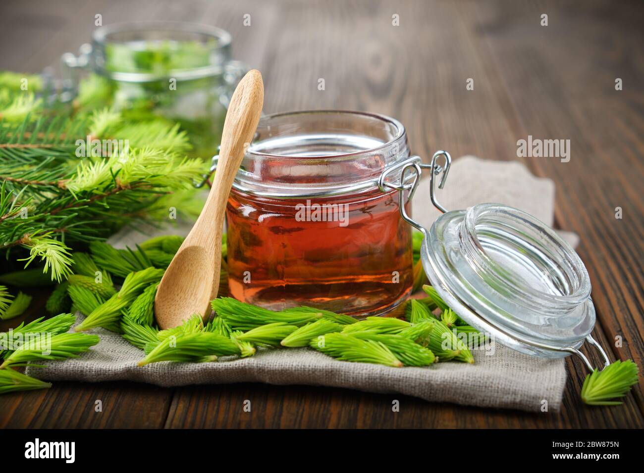Jar of  jam, syrup or honey from fir buds and needles, twigs of fir tree on wooden table. Making spruce tips jam at home. Stock Photo