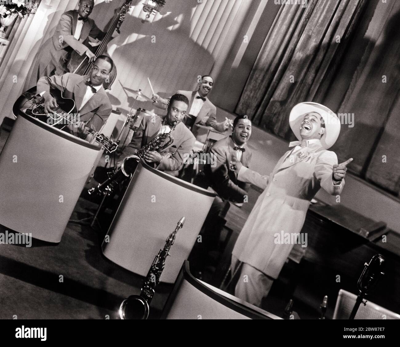 1940s SINGER BANDLEADER AFRICAN AMERICAN CAB CALLOWAY AND FIVE ORCHESTRA MUSICIANS IN PUBLICITY MOVIE STILL FROM STORMY WEATHER - asp fwp1976 ASP001 HARS FILM ROMANCE COMMUNITY URBAN OLD TIME NOSTALGIA OLD FASHION 1 STYLE COMMUNICATION CAREER INSTRUMENTS SINGER TEAMWORK JOY LIFESTYLE ACTOR FIVE HISTORY CELEBRATION CAB 5 JOBS UNITED STATES COPY SPACE FULL-LENGTH HALF-LENGTH DRUMS PERSONS INSPIRATION UNITED STATES OF AMERICA MALES PROFESSION ENTERTAINMENT JIVE STORMY B&W MOVIES MUSICIANS NORTH AMERICA EYE CONTACT NORTH AMERICAN PERFORMING ARTS WIDE ANGLE SKILL OCCUPATION HAPPINESS SKILLS FILMS Stock Photo
